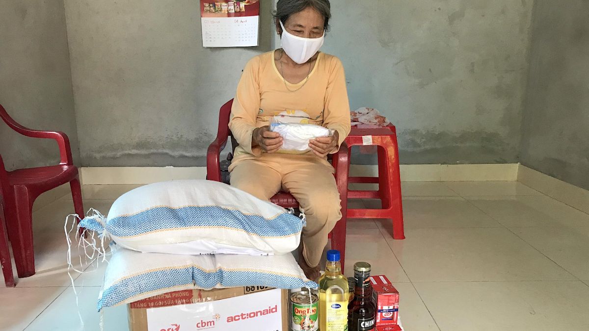Eine Frau aus Asien sitzt vor einem Paket, auf dem zwei Säcke liegen. Daneben stehen Flaschen mit Öl und andere Lebensmittel.