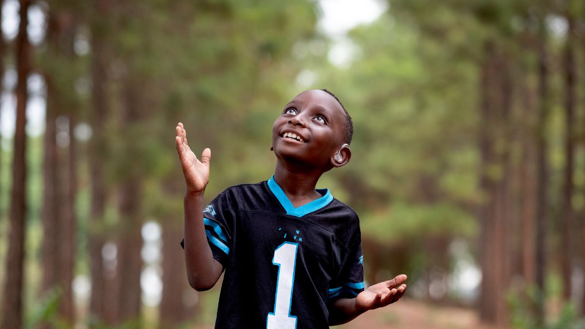 Ein Junge steht unter Bäumen, blickt nach oben und scheint zu lauschen.