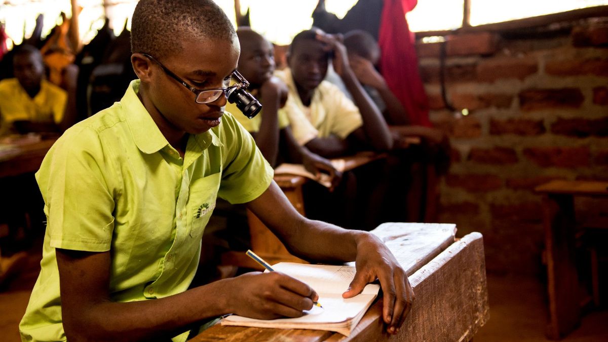 Afrikanischer Jugenlicher mit Brille und Lupe in einem Klassenzimmer