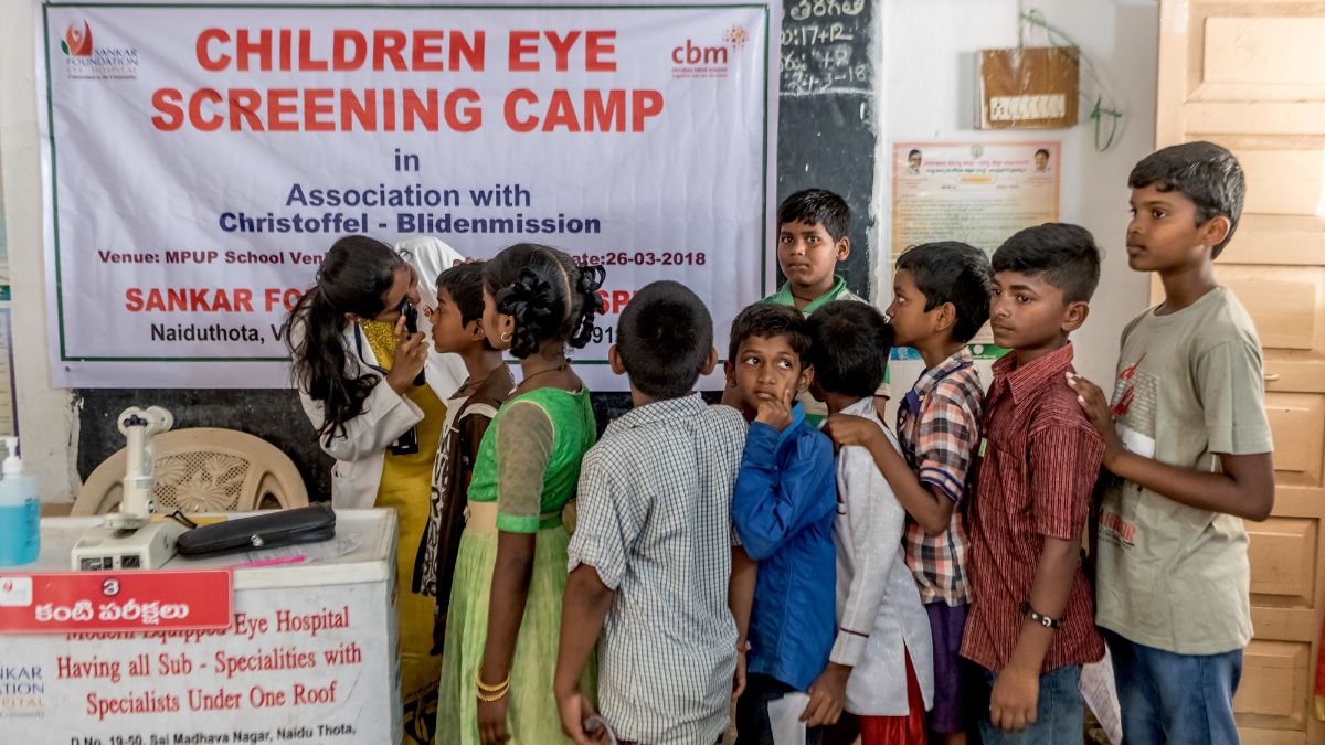 Indische Kinder warten in einer Schlange auf ihre Augenvorsorgeuntersuchung.