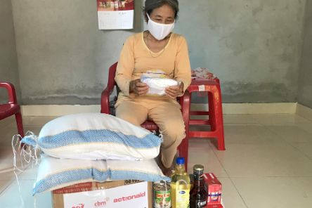 Eine Frau aus Asien sitzt vor einem Paket, auf dem zwei Säcke liegen. Daneben stehen Flaschen mit Öl und andere Lebensmittel.