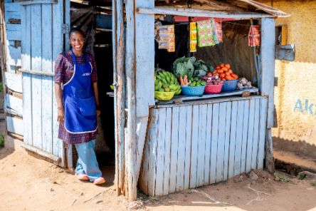 Eine junge Frau steht im Türrahmen ihres Marktstandes und lächelt in die Kamera.