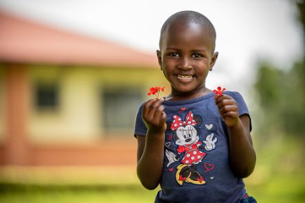 Ein kleines Mädchen hält in beiden Händen rote Blümchen.