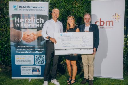 Ein Mann, eine Frau und noch ein Mann blicken in die Kamera. Sie halten einen großen Scheck in den Händen. Hinter ihnen zwei Rollups: Dr. Schlemann steht auf dem einen, auf dem anderen CBM.