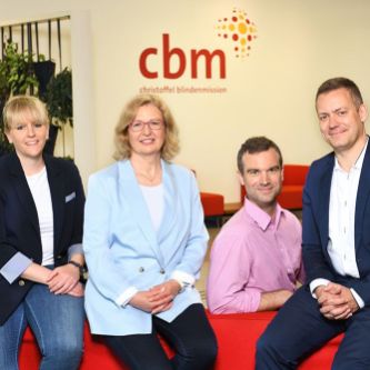 Gruppe von zwei Männern und zwei Frauen, drei der Personen sitzen auf einer Sofalehne.