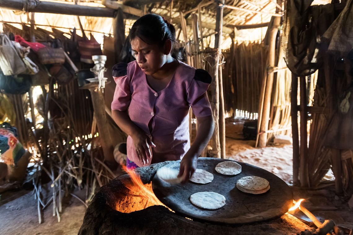 Eine junge blinde Frau aus Guatemala backt auf einem Lehmofen in ihrer Hütte Tortillas.
