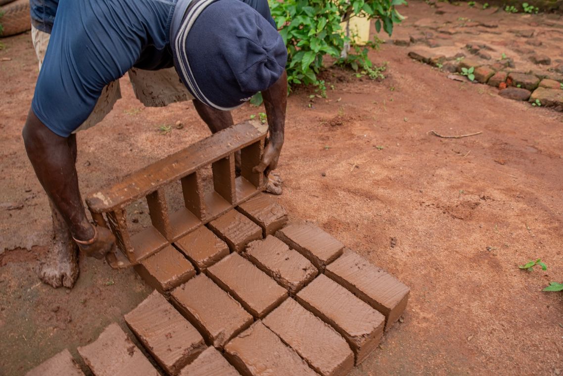 Ein Mann mit Mütze hat aus einer Holzform Backsteine auf den Boden gekippt.