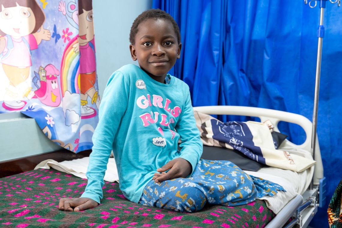 Ein Mädchen sitzt auf einem Krankenhausbett.