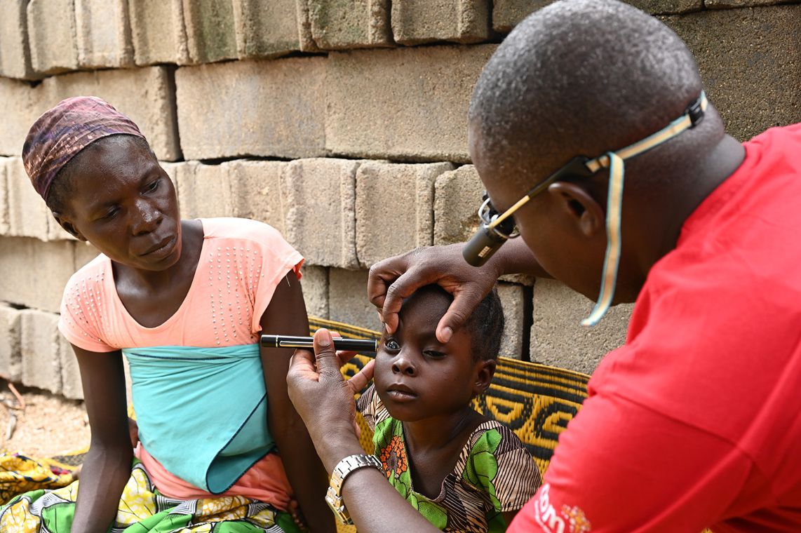 Ein Mann leuchtet mit einer Handlampge in die Augen eines etwa achtjährigen Mädchens.
