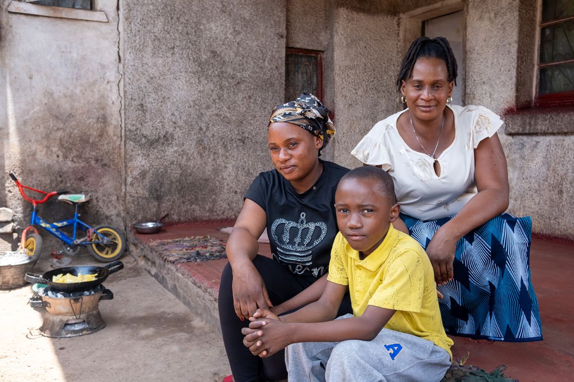 Ein Junge sitzt zwischen zwei Frauen auf der Veranda eines kleinen Hauses.
