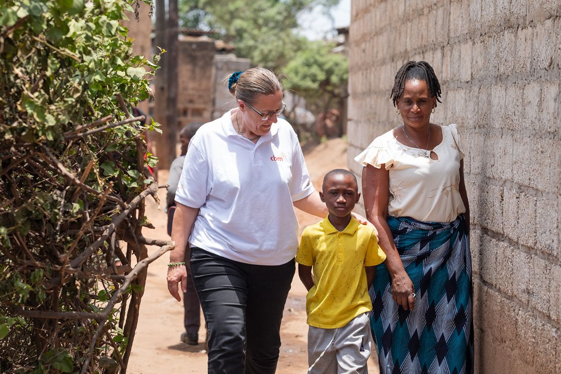 Ein Junge sitzt zwischen zwei Frauen auf der Veranda eines kleinen Hauses.