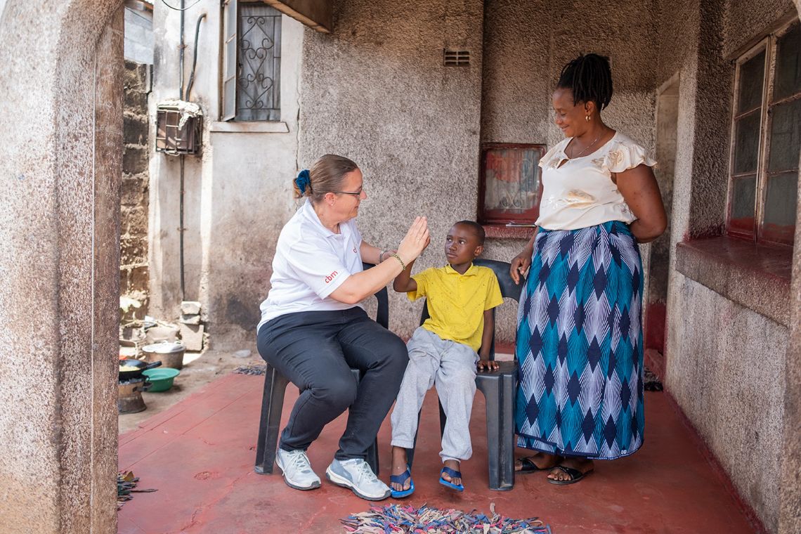 Eine Frau im weißen Polohemd und ein kleine Junge klatschen einander auf die Hand. Eine weitere Frau mit buntbedrucktem Rock steht dabei.