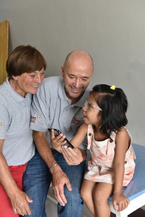 Ein Mann und eine Frau schauen zusammen mit einem Kind mit Brille auf ein Handy
