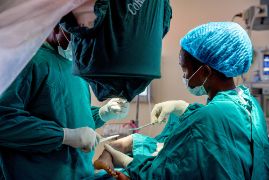 Ein kleines afrikanisches Mädchen mit extremen O-Beinen lehnt sich an einen Baumstamm.
