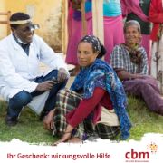 Afrikanischer Mann mit weißem Kittel und Stirnlampe und eine afrikanische Frau sitzen auf einem Rasen.