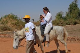 Eine Frau und ein kleines Kind reiten auf einem Pferd, das von einem Mann geführt wird