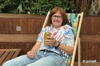 Eine Frau im Liegestuhl hält ein Trinkgefäß mit Stohhalm in der Hand.