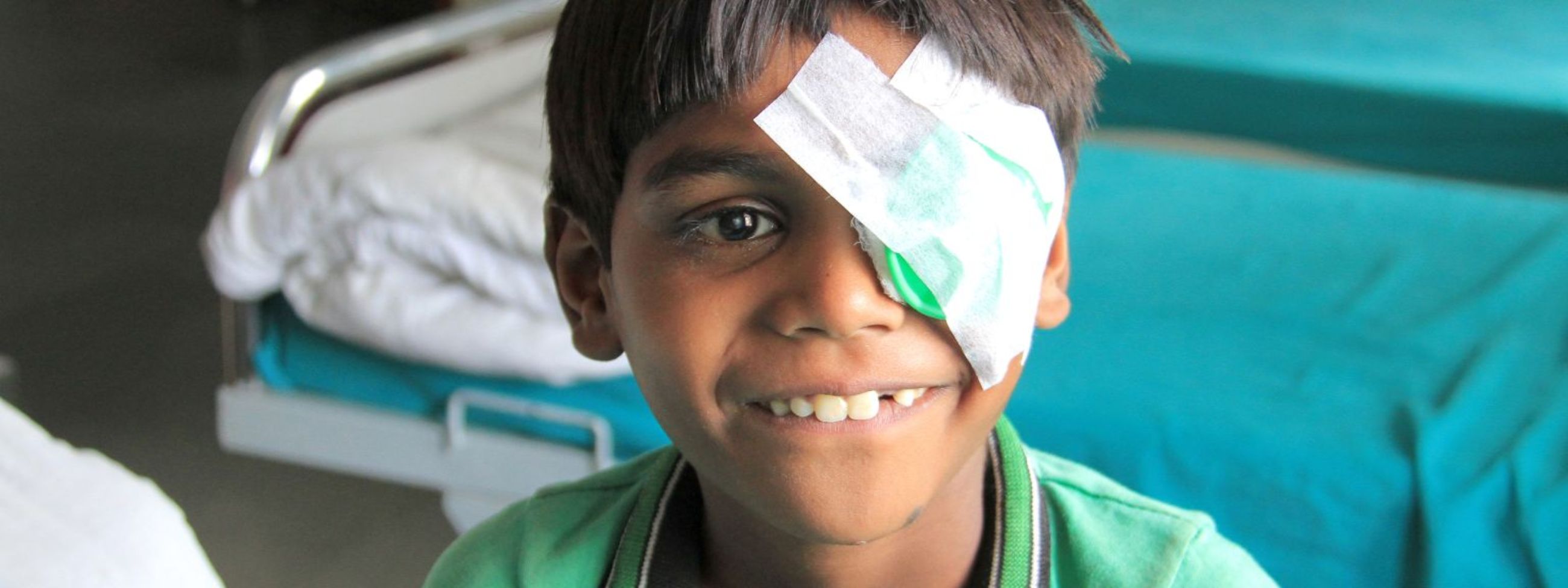 Der sechsjährige Gokul aus Indien trägt einen Tag nach seiner Grauer Star-OP eine Augenklappt und lächelt fröhlich.