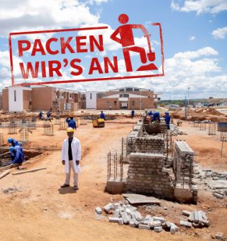 Ein Mann im weißen Kittel und mit Bauhelm steht auf einer Baustelle