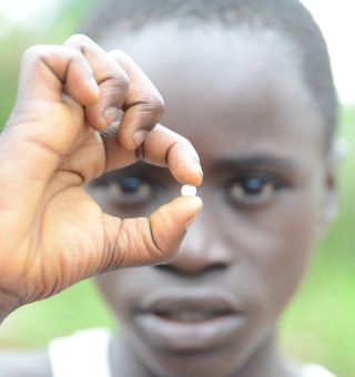 Ein afrikanisher Junge hält eine kleine Tablette zwischen den Fingern und hält sie vor sein Gesicht.