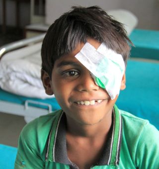 Der sechsjährige Gokul aus Indien trägt einen Tag nach seiner Grauer Star-OP eine Augenklappt und lächelt fröhlich.