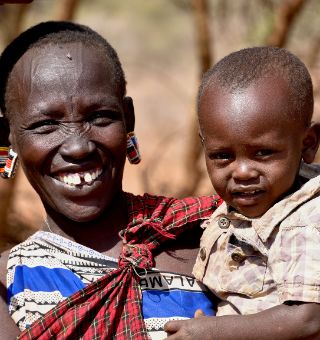 Eine lächelnde afrikanische Frau hat ein Kleinkind auf dem Arm.