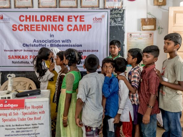 Indische Kinder warten in einer Schlange auf ihre Augenvorsorgeuntersuchung.