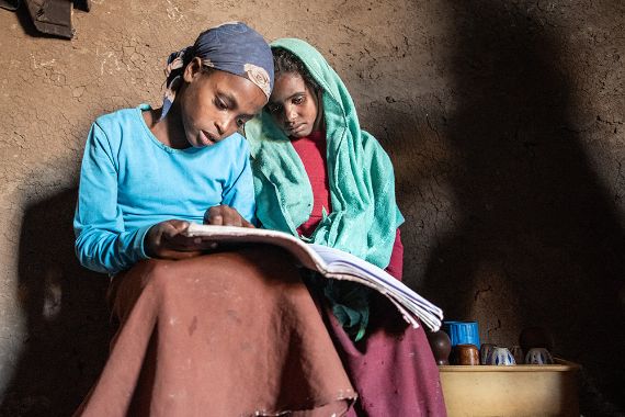 Zwei Mädchen sitzen aneinandergeschmiegt und haben auf dem Schoß ein aufgeschlagenes Buch.