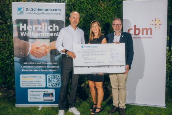 Ein Mann, eine Frau und noch ein Mann blicken in die Kamera. Sie halten einen großen Scheck in den Händen. Hinter ihnen zwei Rollups: Dr. Schlemann steht auf dem einen, auf dem anderen CBM.