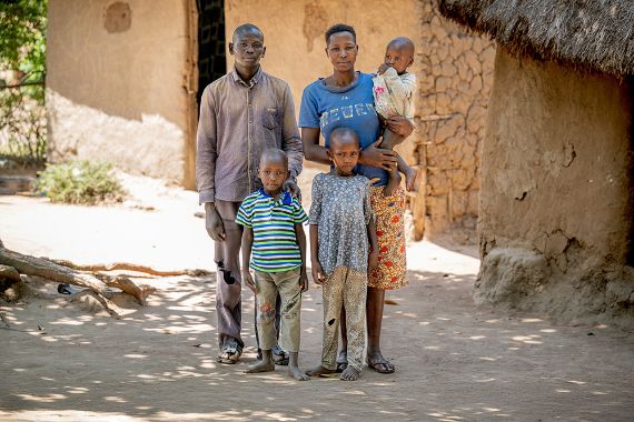 Ein Mann, eine Frau mit Baby auf dem Arm und zwei Kinder stehen vor einer strohgedeckten Lehmhütte.