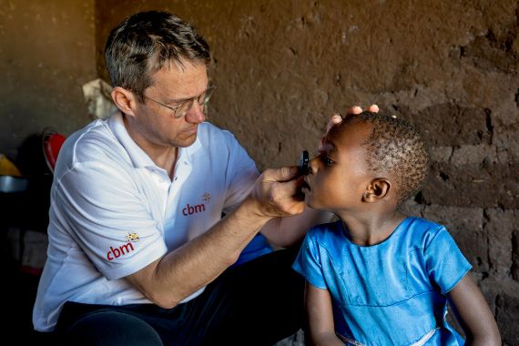 Ein Mann untersucht mit einer Handlampe die Augen eines etwa fünfjährigen Mädchens.