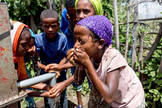 Kinder waschen sich an einem Wasserhahn das Gesicht.