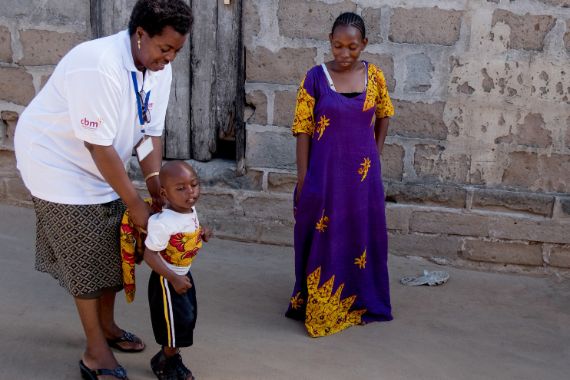 Eine afrikanische Projektmitarbeiterin trainiert das Laufen mit einem an körperbehinderten Kind