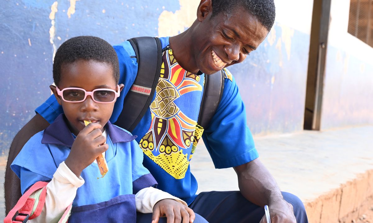 Ein lachender Mann und ein kleines Mädchen mit Brille sitzen an einer Hauswand.