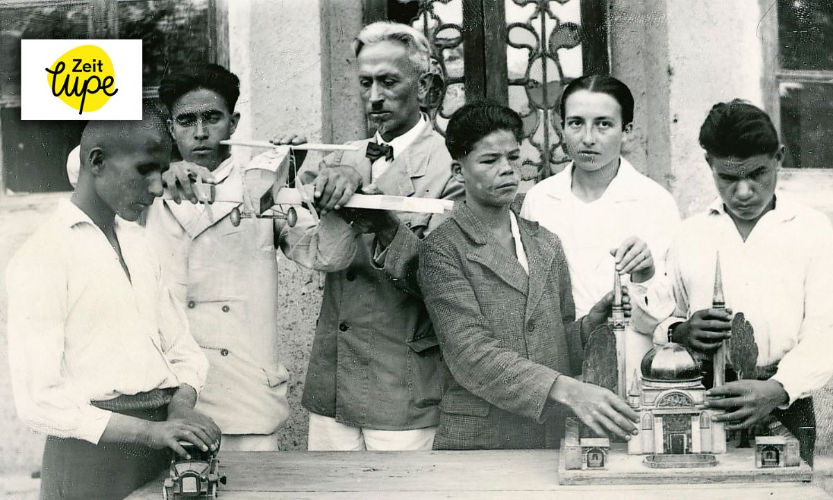 Ein Mann, eine Frau und einige Jugendliche betasten ein Flugzeugmodell und das Modell  eines Gebäudes; in der Mitte ein Video-Play-Button