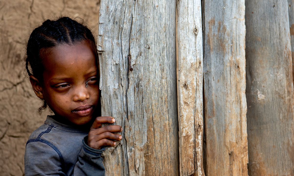 Ein etwa fünfjähriges Mädchen schaut hinter dem Türrahmen eines Hütteneingangs hervor.